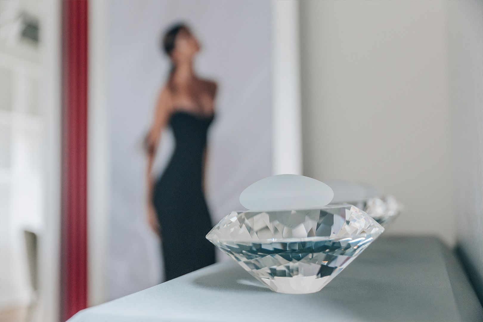 Brustimplantat auf Diamant, im Hintergrund Frau in schwarzem Abendkleid