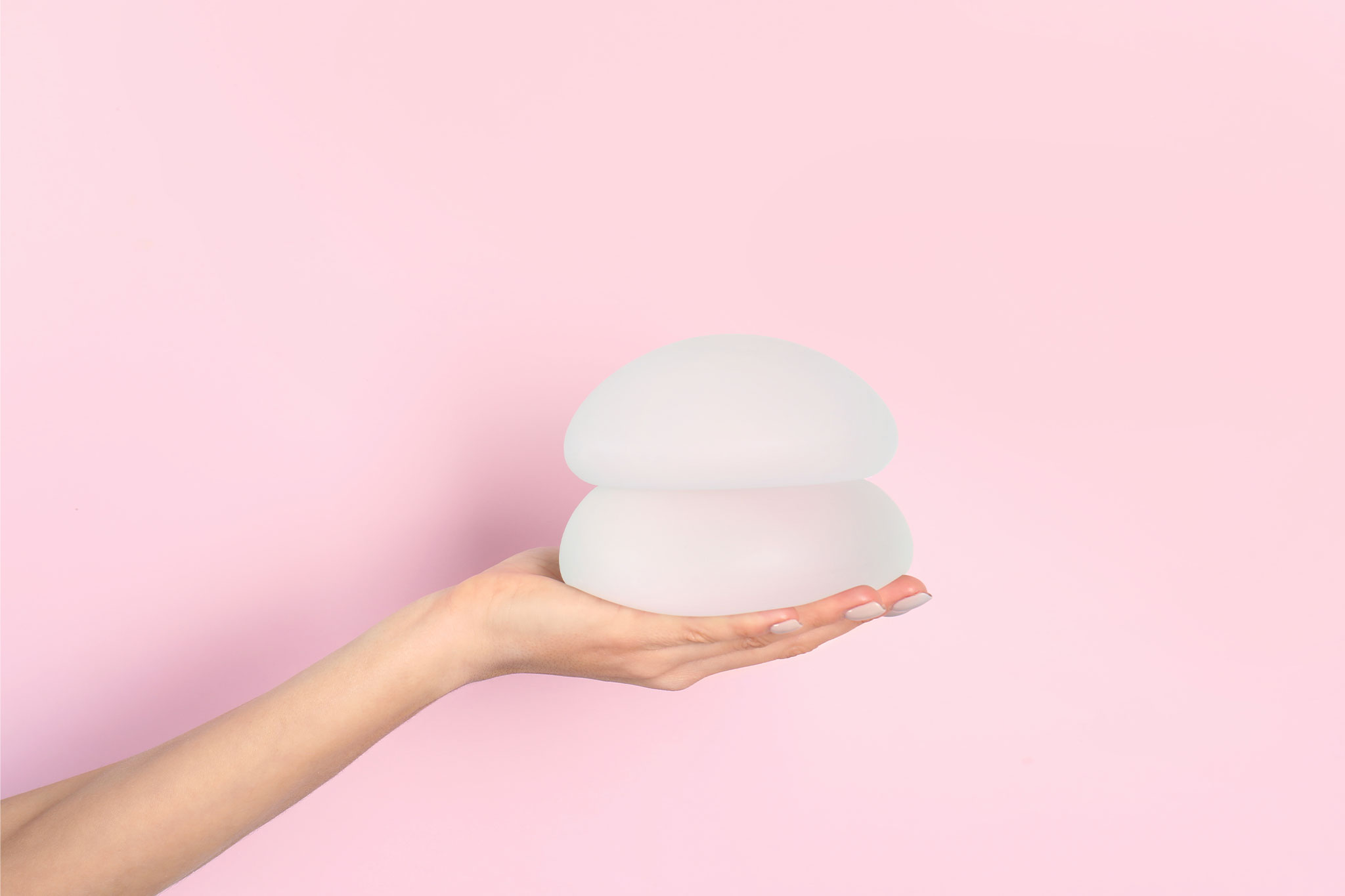 Hand, die Brustimplantate hält, symbolisiert Grösse und Form von Brustimplantaten